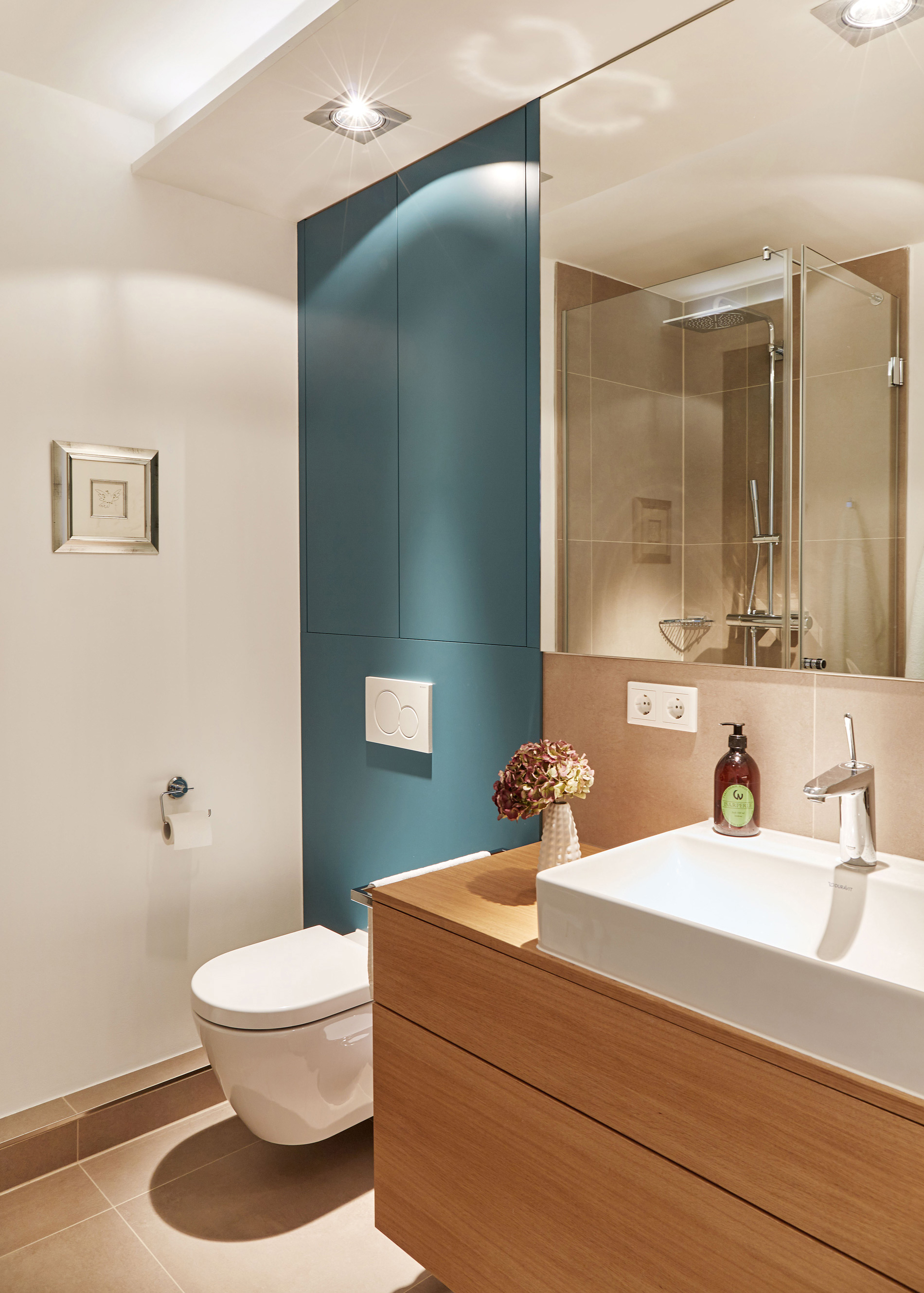 Foto: Modernes Badezimmer mit Toilette und Waschtisch aus Holz, Spiegel, integrierten Deckenspots und dunkelblauer Akzentwand.