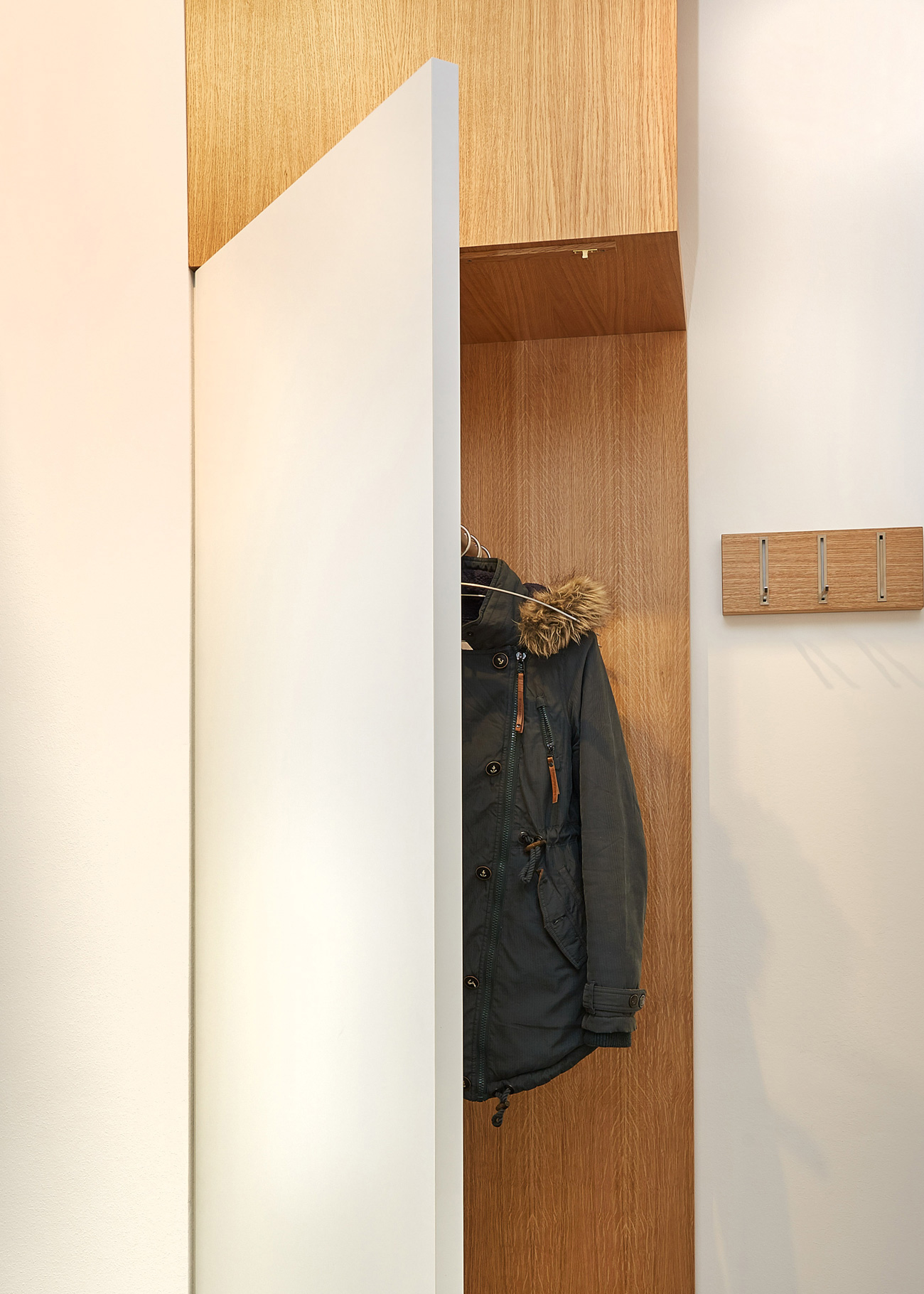 Foto: Detailaufnahme Einbaugarderobenschrank aus Holz mit weißer aufgeklappter Tür, integrierter Beleuchtung und Kleiderhaken.