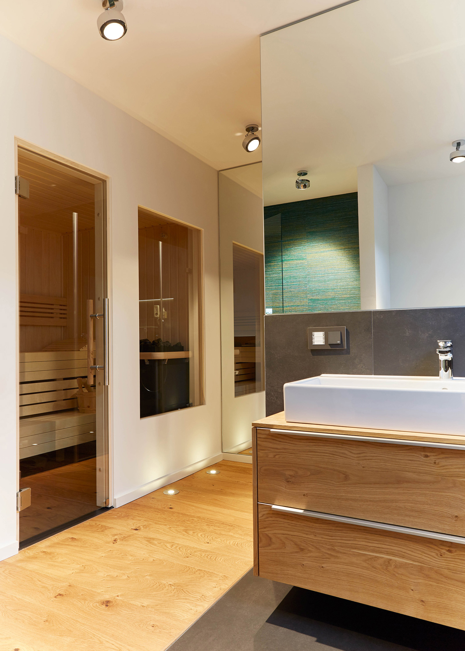 Foto: Hochwertiger, luxuriöser Home Spa Bereich mit durch Glastüren abgetrennter Sauna und Waschbecken in warmen Naturmaterialien, moderne indirekte Beleuchtung.