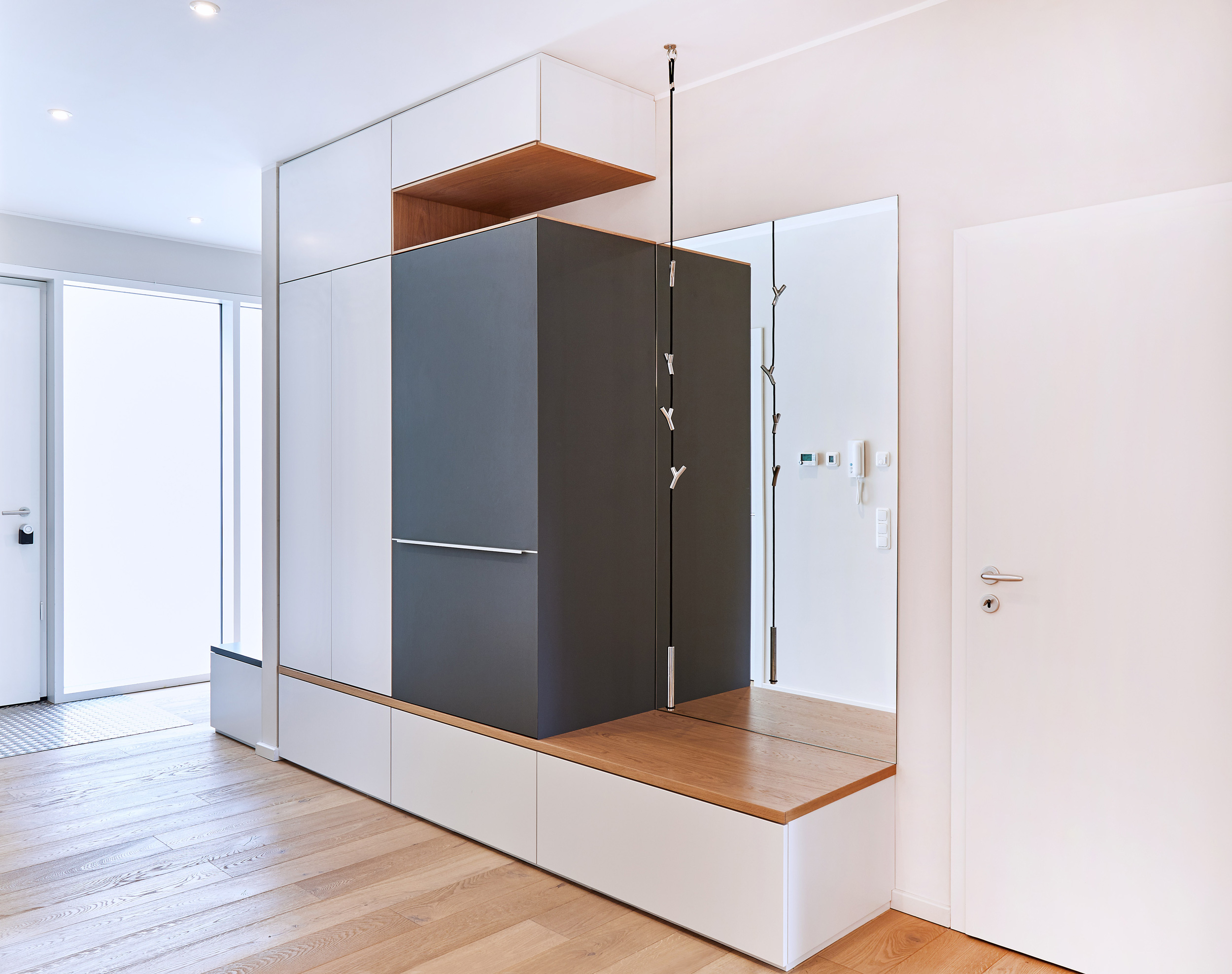 Foto: Raumbildender Garderobenschrank im Eingangsbereich mit Kleiderharken und Spiegel, aus schwarzen, weißen und Naturholz Elementen.