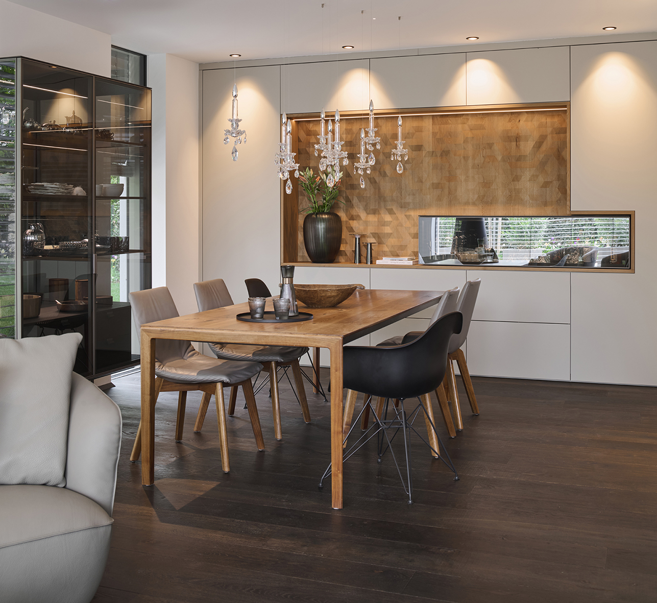 Foto: Moderner Essbereich mit dunklem Holzboden, Holztisch, hochwertigen Stühlen, Kronleuchter und weißer Regalwand mit integrierter Vitrine und geometrischer Holzvertäfelung.