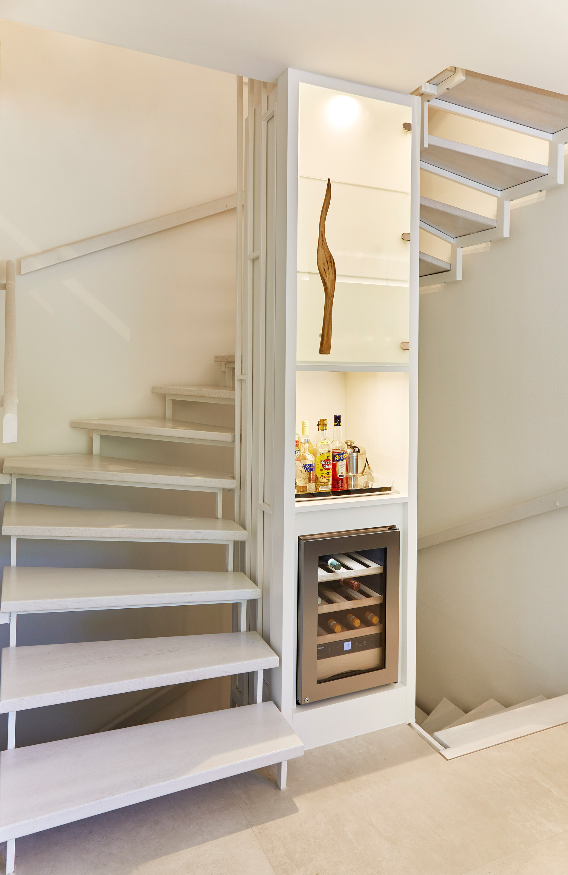 Foto: Weiße, gewendelte, Treppe mit offenen Stufen. Mittelsäule der Treppe bildet ein bezieht beleuchteter Schrank mit integriertem Weinkühlschrank und Hausbar.