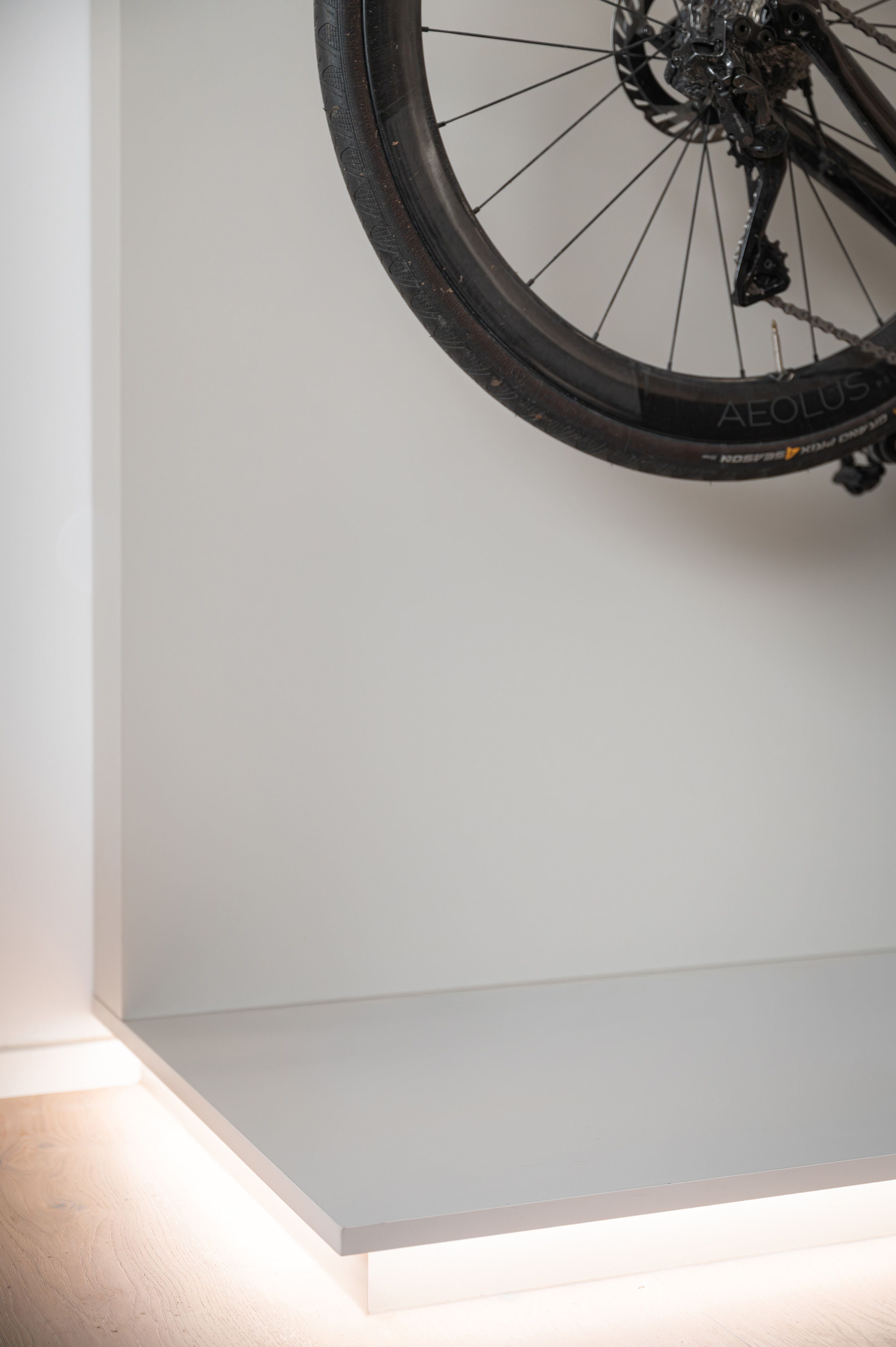 Foto: Detailaufnahme weißer, moderner Sockel mit indirekter Unterbeleuchtung für darüber aufgehängte, inszenierte Rennräder.