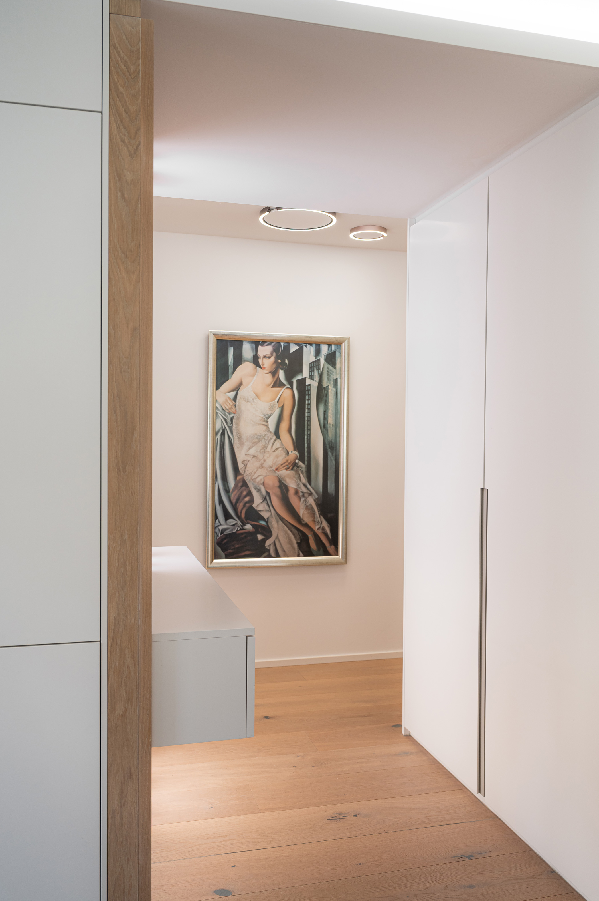 Foto: Moderner Flur mit hellem Holzboden, weißen raumhohen Einbauschränken, indirekter Beleuchtung, runder Deckenleuchte und modernem, expressionistischem Wandgemälde.