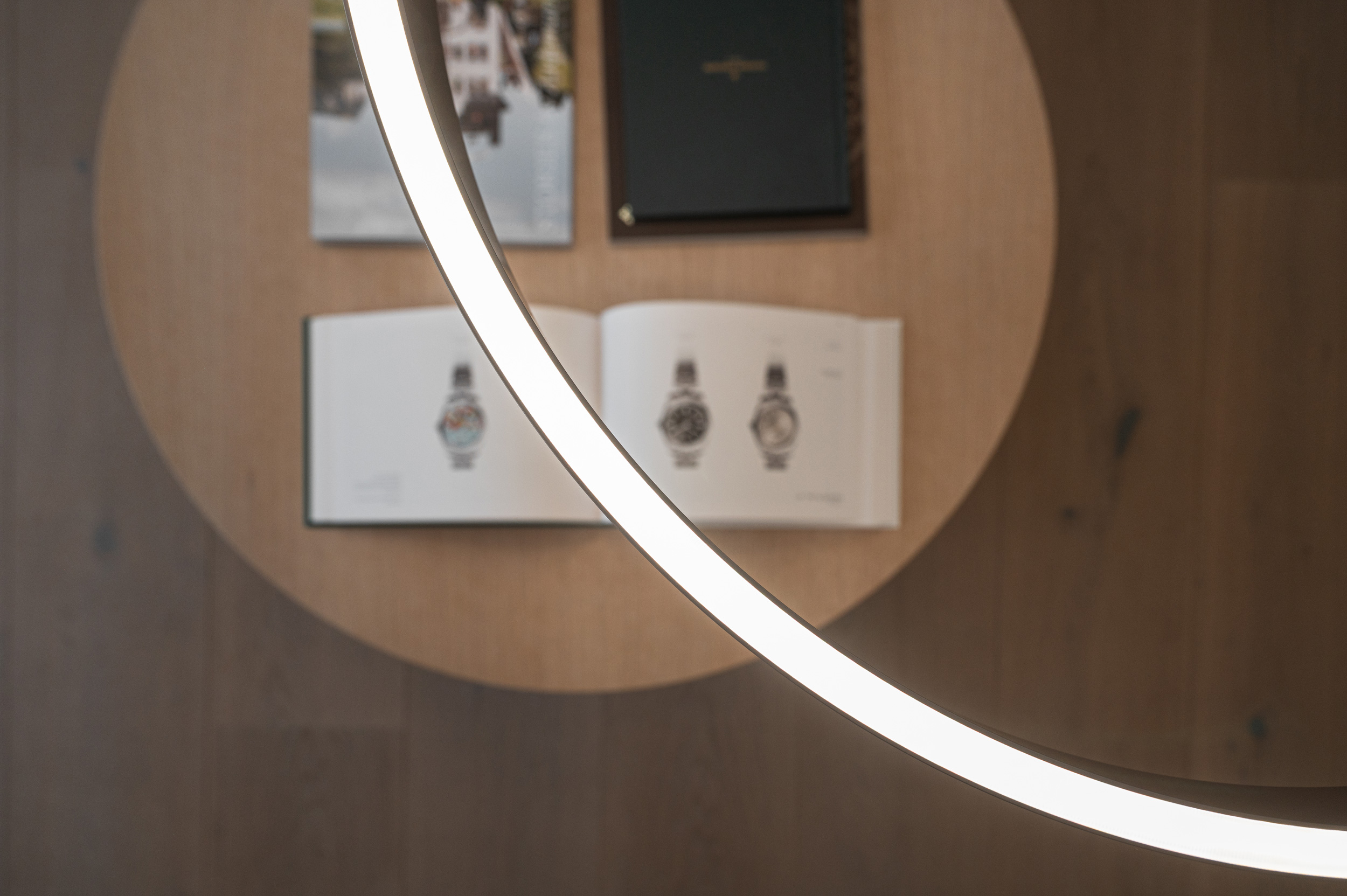 Foto: Detailaufnahme von oben, moderne ringförmige Pendelleuchte, im unscharfen Hintergrund Couchtisch mit hochwertigen Katalog Büchern.